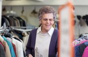 Foto: Eine Seniorin in einer Kleiderkammer - im Vordergrund ein Schild.